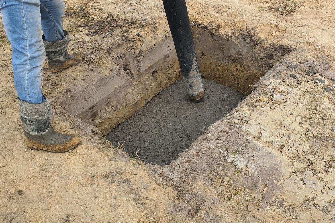 Concrete being placed by hose into foundation formwork with rebar reinforcement in place.